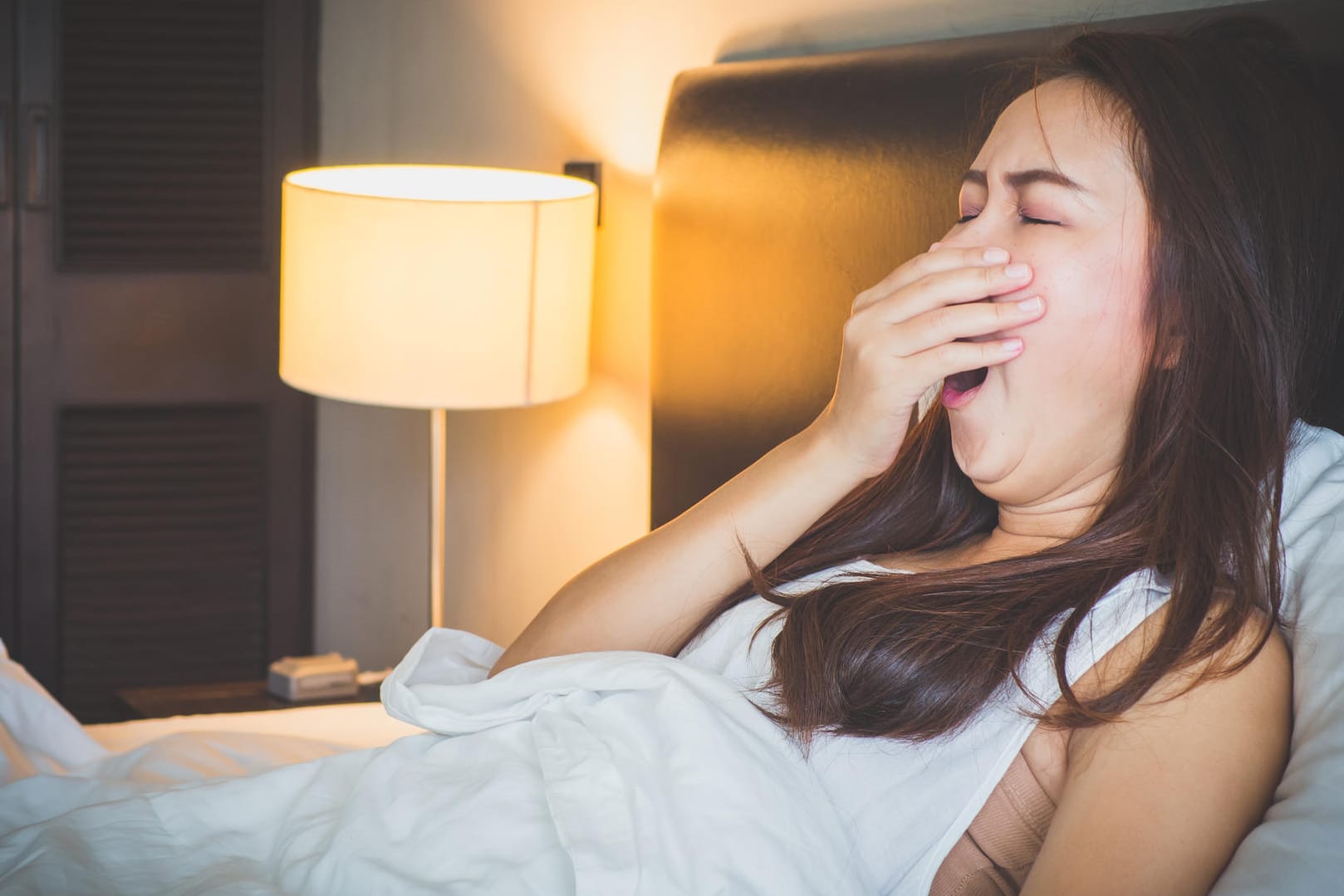 Eine junge Frau sitzt gähnend im Bett: Mit einer Tageslichtlampe lässt sich die Herbstmüdigkeit bekämpfen.