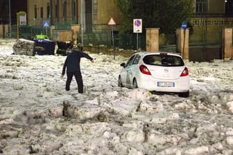 Ein Mann versucht in Rom ein durch Hagelmassen blockiertes Auto zu erreichen.