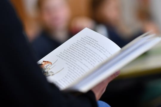 Eine Lehrerin liest in einer Grundschule in ihren Drittklässlern aus einem Buch vor.