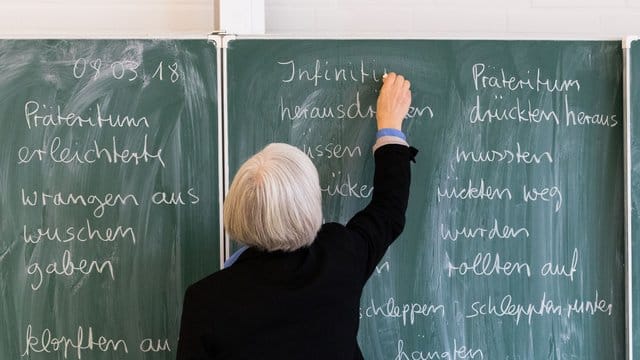 Eine Lehrerin steht in einem Klassenraum.