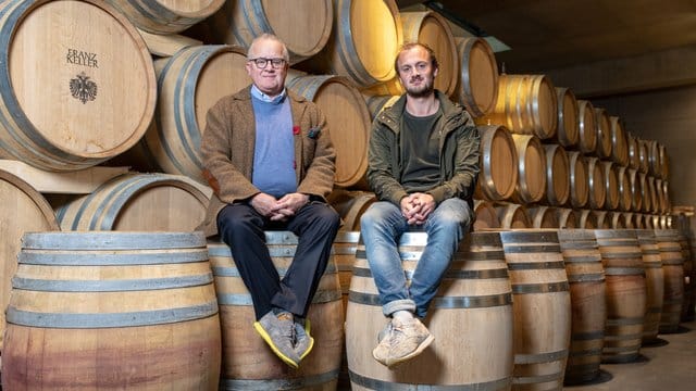 Die Winzer Fritz (l) und sein Sohn Friedrich (r) Keller sitzen im Weingut auf Weinfässern.