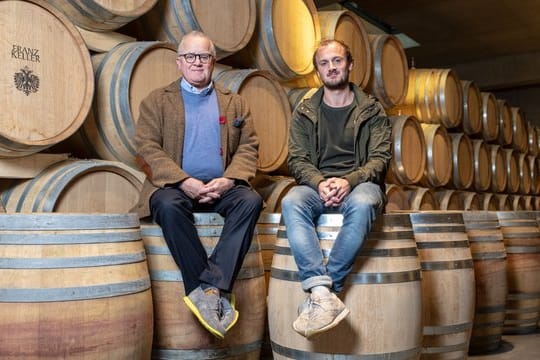 Die Winzer Fritz (l) und sein Sohn Friedrich (r) Keller sitzen im Weingut auf Weinfässern.