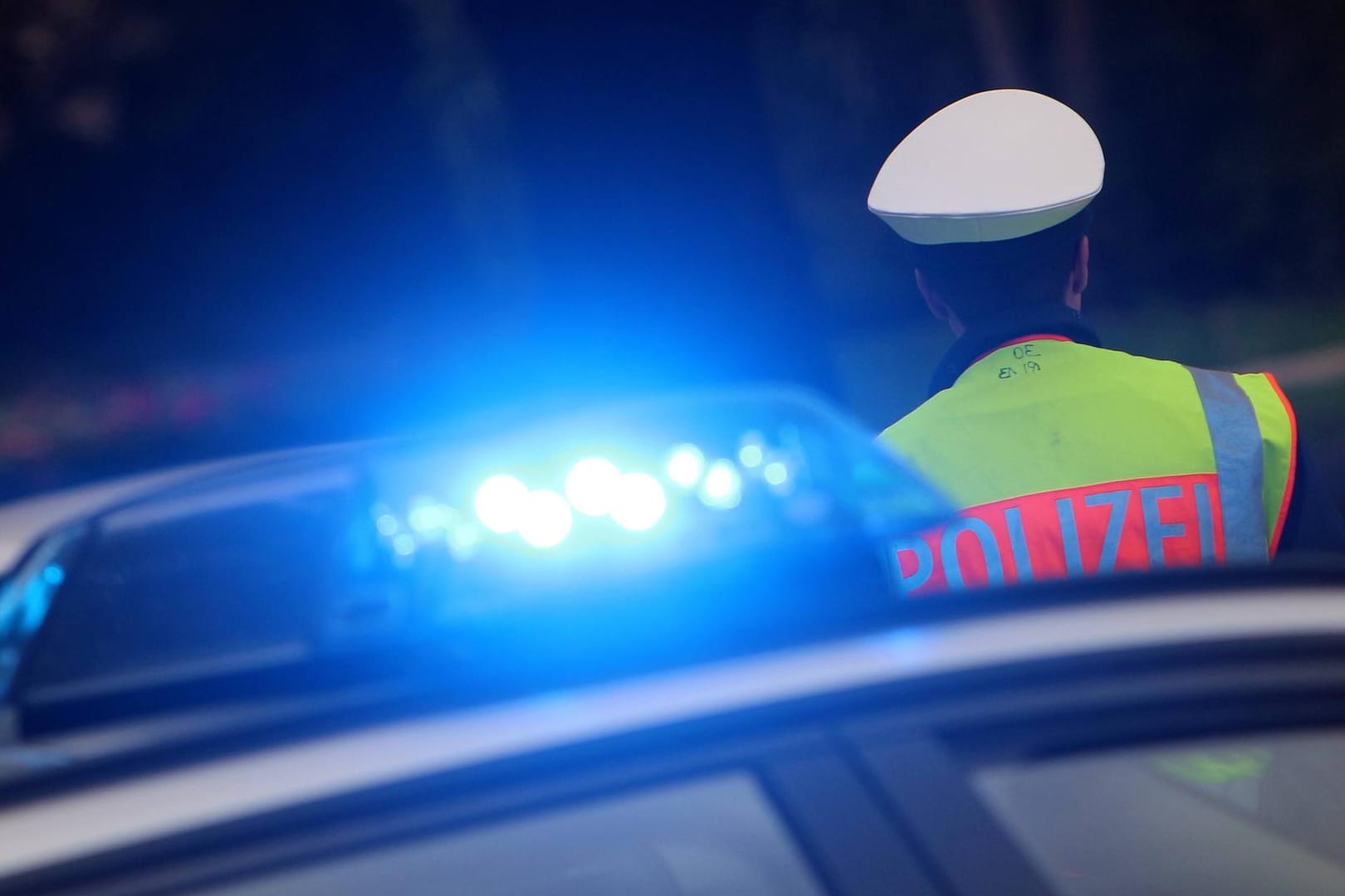Polizist mit Mütze und Warnweste steht neben einem Einsatzwagen der Polizei: Anwohner hatten die Männer bei ihrer Tat beobachtet.
