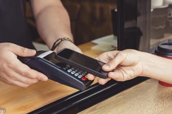 Eine Person bezahlt mit dem Smartphone: Mit Diensten wie Apple Pay können Smartphones die Kreditkarte ersetzen.