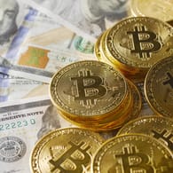 Symbolische Bitcoin-Münzen liegen auf Geldscheinen: Um Bitcoins zu schürfen, werden immer aufwändigere Rechenprozesse nötig – und das verbraucht Energie. (Symbolbild)