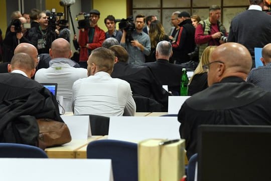 Die Angeklagten und ihre Anwälte sitzen vor Beginn ihres Prozesses in einem Saal in der Siegerlandhalle.