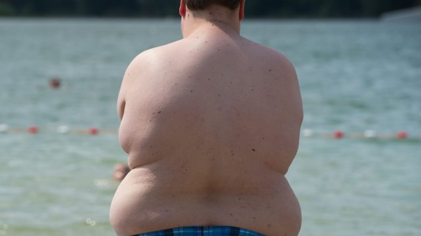 Ein fettleibiger Junge steht an einem Badesee.
