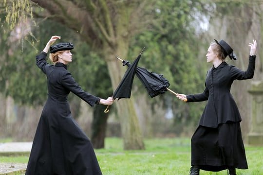 Esther Schweins (l) in der Rolle von Emmeline Pankhurst und Anke Retzlaff als ihre Tochter Christabel kämpfen mit Regenschirmen.