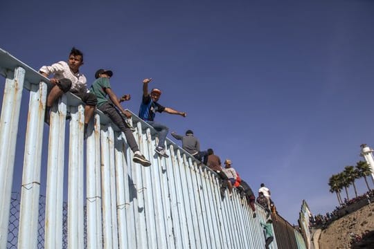 Migranten aus Mittelamerika sitzen in Tijuana auf dem Grenzzaun zwischen Mexiko und den USA.
