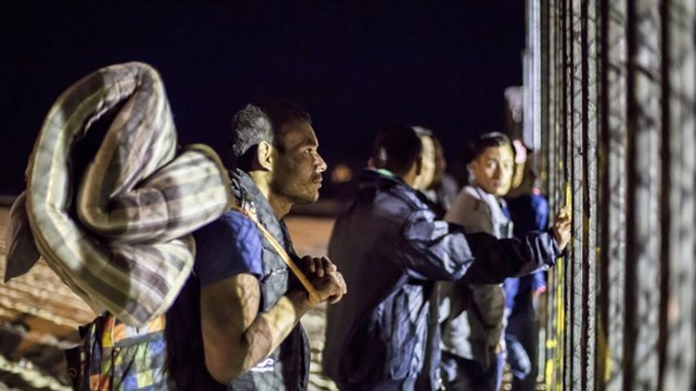 Migranten mit Matratzen und Rucksäcken am Zaun der Grenze zwischen USA und Mexiko.