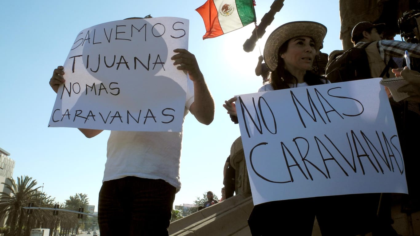 Protest in Tijuana: Eine Demonstrantin steht mit einem Schild "No mas Caravanas" ("Keine Karawanen mehr") bei einer Demonstration gegen Migranten. Links ein Demonstrant mit einem Schild "Lass uns Tijuana retten – Keine Karawanen mehr".