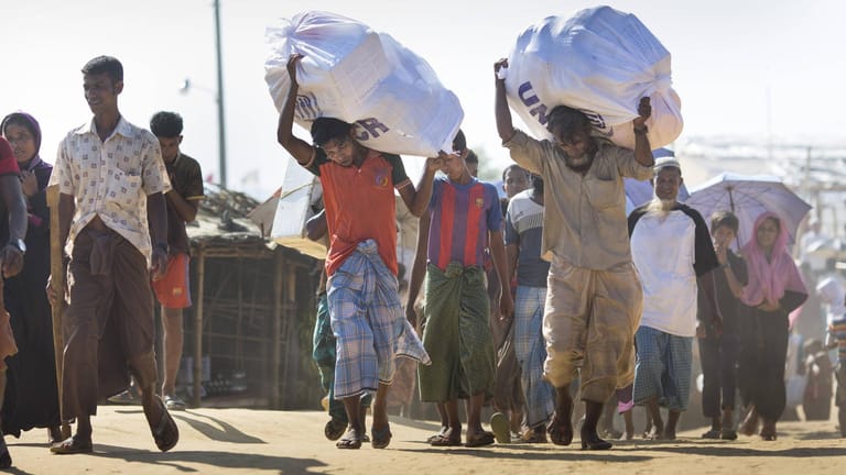 Männer tragen Hilfsgüter des UNHCR im Flüchtlingslager Kutupalong, in dem Rohingya, die aus Myanmar vertrieben wurden, leben: Der UN-Migrationspakt soll die Lage der Flüchtlinge weltweit verbessern.