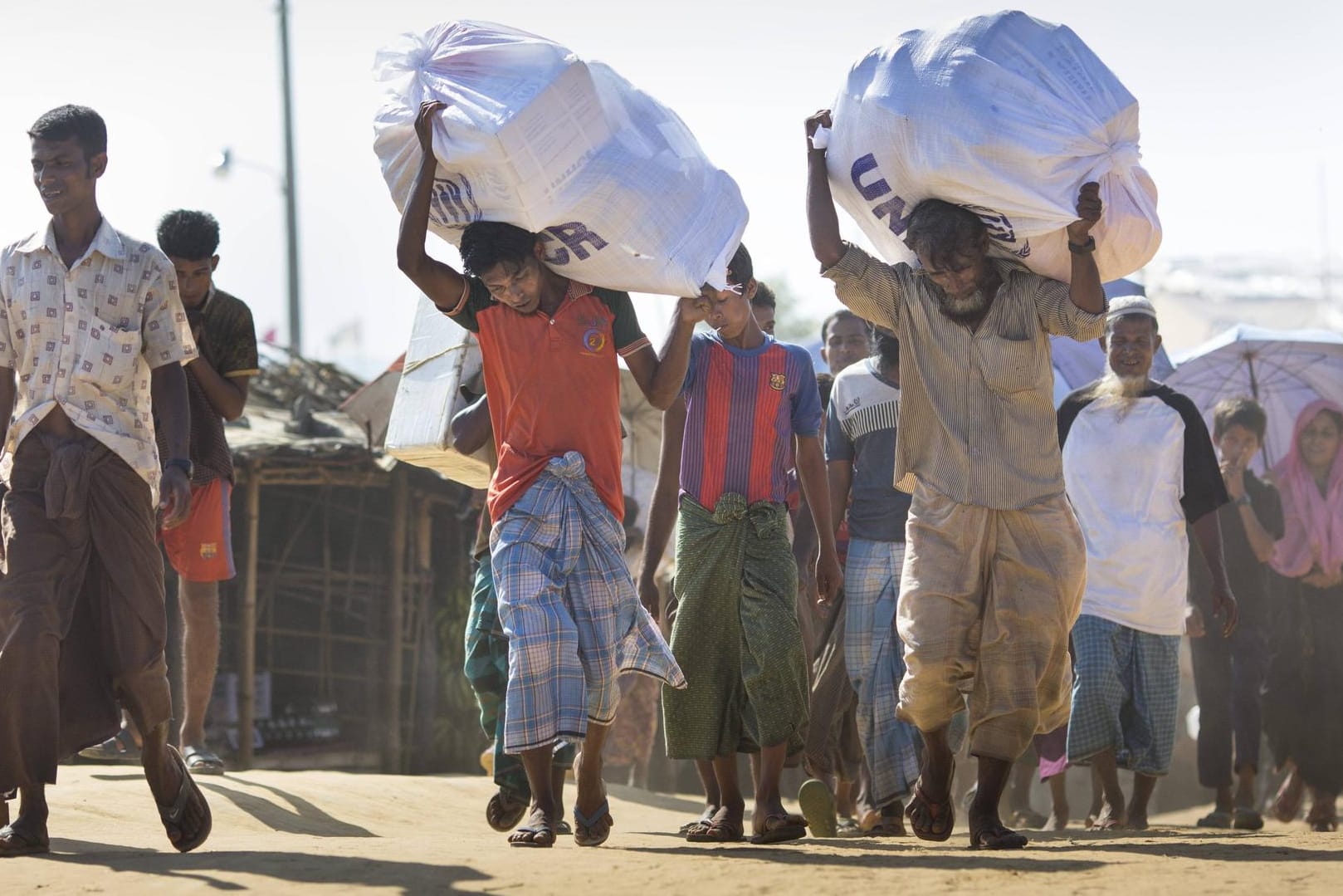 Männer tragen Hilfsgüter des UNHCR im Flüchtlingslager Kutupalong, in dem Rohingya, die aus Myanmar vertrieben wurden, leben: Der UN-Migrationspakt soll die Lage der Flüchtlinge weltweit verbessern.