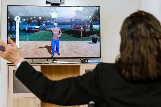 Eine Pflegeheimbewohnerin steuert in einem therapeutischen Videospiel aus dem Rollstuhl heraus ihren Avatar durch Armbewegungen.