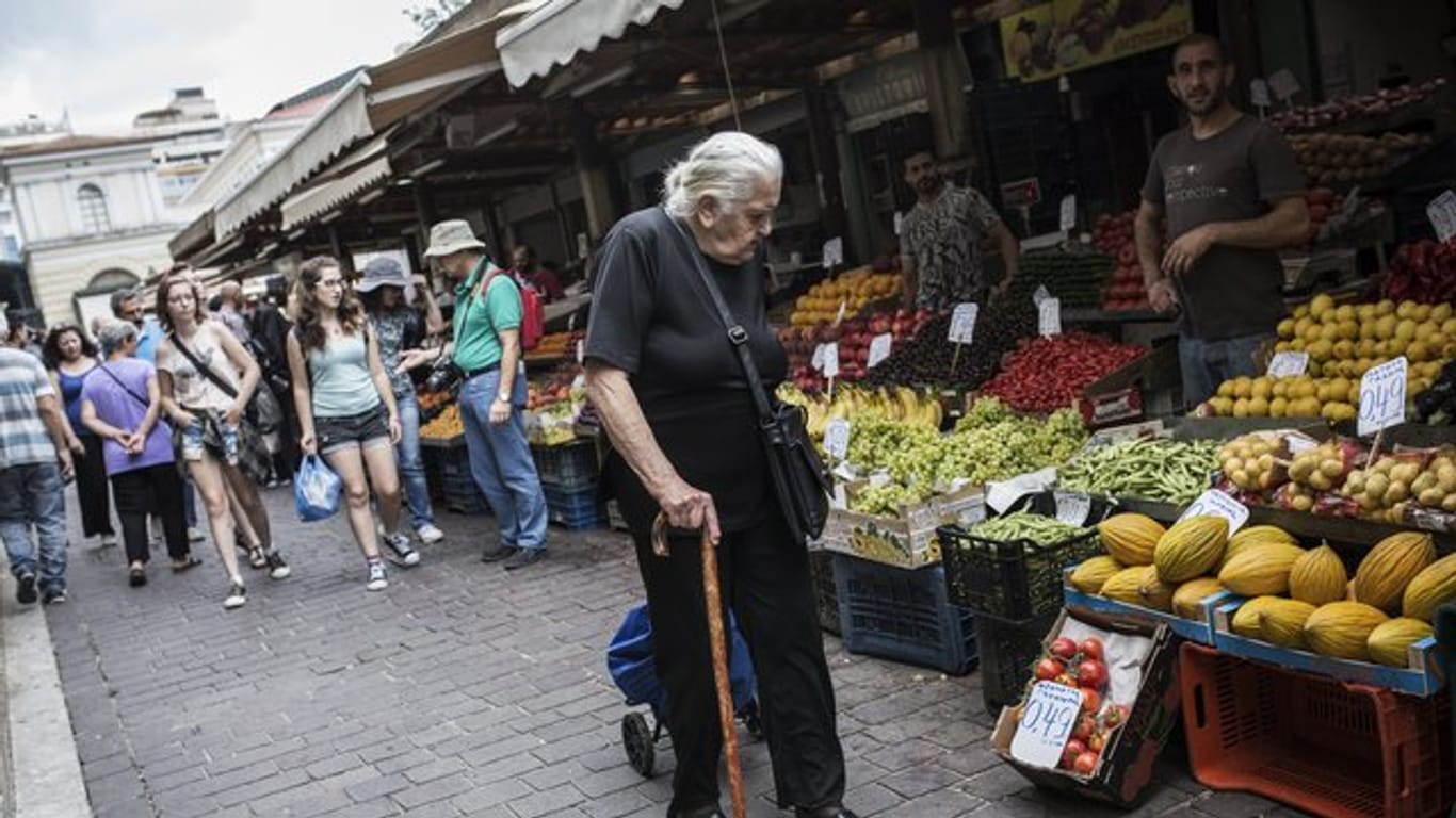 Eine ältere Frau geht in Athen an Marktständen vorbei.