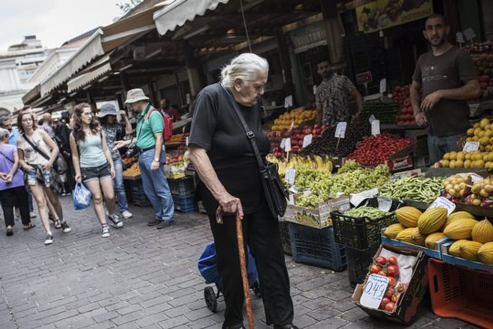 Eine ältere Frau geht in Athen an Marktständen vorbei.