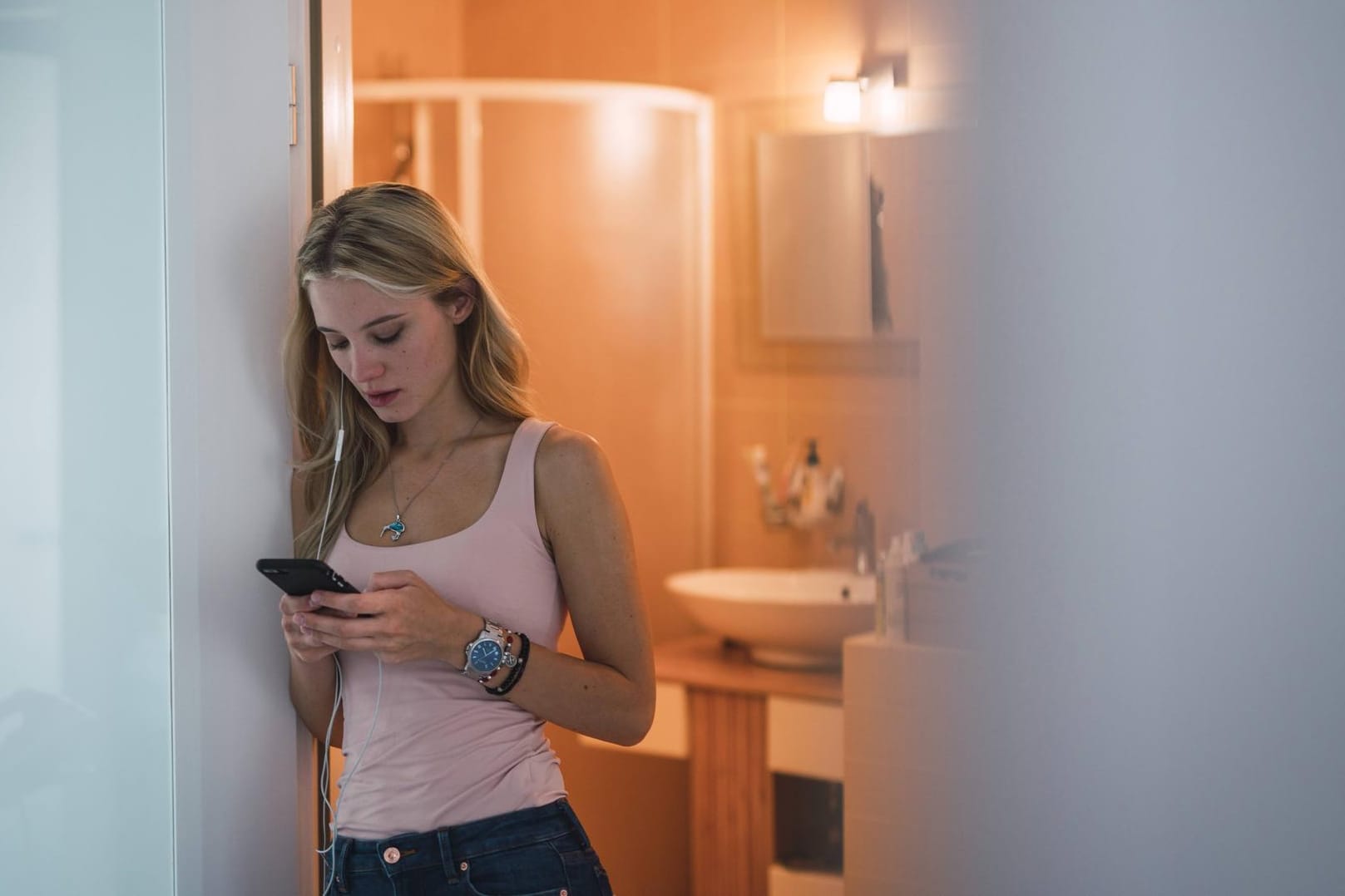 Eine junge Frau steht in der Badezimmer-Tür und schaut auf ihr Smartphone: Viele Smart Home-Geräte sind laut BSI nicht ausreichend gegen Schadsoftware geschützt.