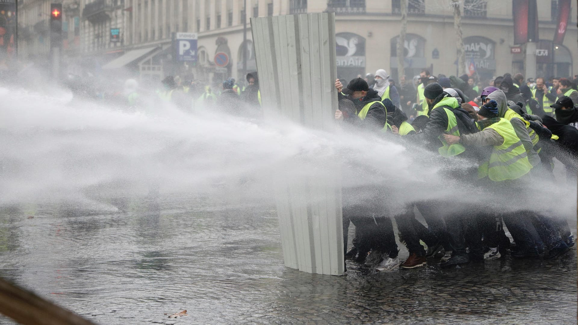 Demonstranten schützen sich mit einer Blechwand vor den Wasserwerfern der Polizei: Seit einer Woche errichten die sogenannten "Gelbwesten" Blockaden im ganzen Land.