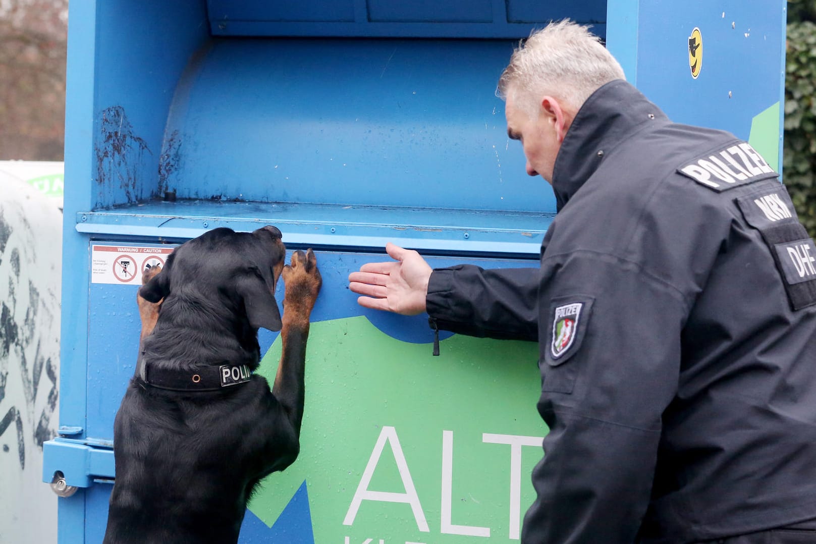Polizeispürhund "Amigo" und ein Polizist suchen nach Spuren an einen Altkleidercontainer: Beim Sortieren von Altkleidern aus Duisburg ist in Polen die Leiche eines Babys gefunden worden.