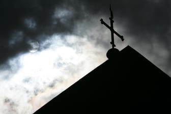 Dunkle Wolken über einer Kirchturmspitze (Symbolbild): Die Staatsanwaltschaft wirft einem 65 Jahre alten Diakon Vergewaltigung einer 15-Jährigen vor.