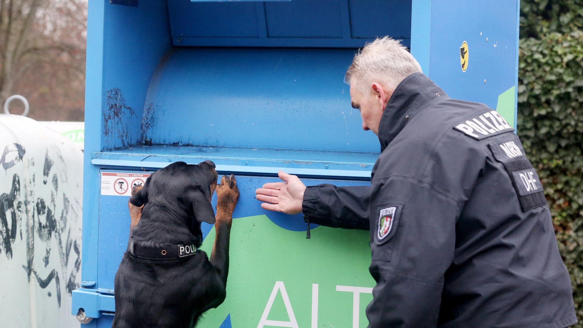 Polizeispürhund "Amigo" und ein Polizeihundeführer suchen nach Spuren an einem Altkleidercontainer: Beim Sortieren von Altkleidern aus Duisburg ist in Polen die Leiche eines neugeborenen Mädchens gefunden worden.