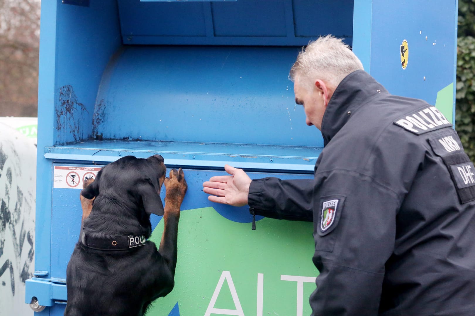 Polizeispürhund "Amigo" und ein Polizeihundeführer suchen nach Spuren an einem Altkleidercontainer: Beim Sortieren von Altkleidern aus Duisburg ist in Polen die Leiche eines neugeborenen Mädchens gefunden worden.