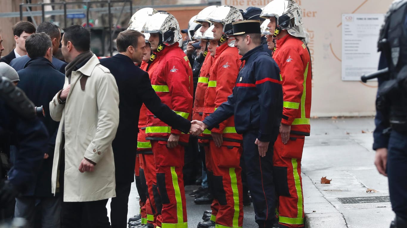 Emmanuel Macron gibt am Tag nach den Ausschreitungen in der Nähe des Arc de Triomphe in Paris einem Feuerwehrmann die Hand.