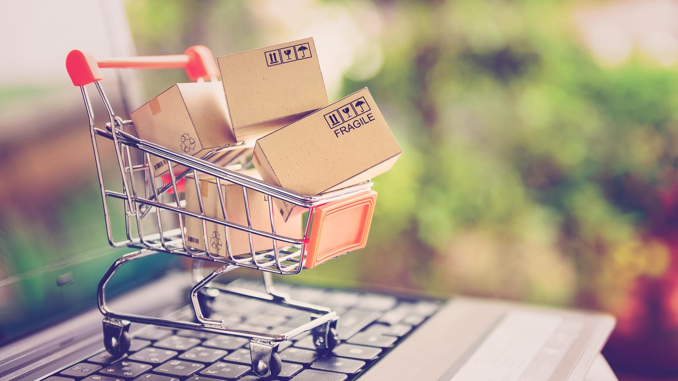 Ein Mini-Einkaufwagen mit Paketen auf einer Tastatur: Ab Montag gelten neue EU-Regeln für Online-Shopping.