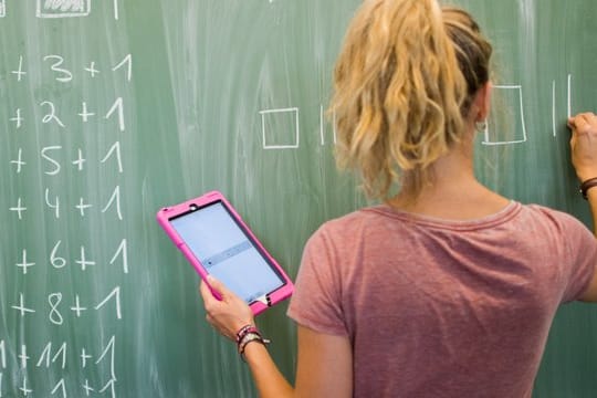 Eine Lehrerin mit Kreide und Tablet im Mathematikunterricht einer 8.