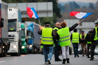 "Gelbwesten" schwenken französische Flaggen auf der Autobahn: Die französische Regierung macht den Demonstranten nun Zugeständnisse.