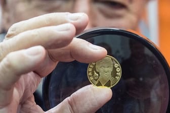 Der Sänger Karel Gott betrachtet mit einer Lupe sein Porträt auf einer Goldmedaille.