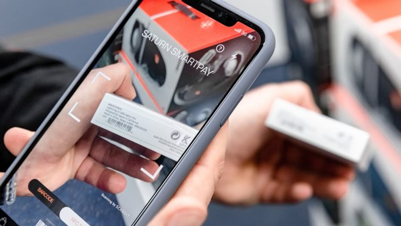 Ein Kunde liest einen Produktpreis aus dem Barcode mit der App "Saturn Smartpay" in sein Handy ein.