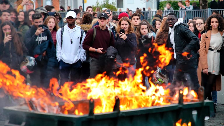 Schüler stehen hinter einer brennenden Mülltonne: Mittlerweile gibt es auch Proteste an französischen Gymnasien. Schüler wehren sich gegen Reformen im Bildungsbereich.