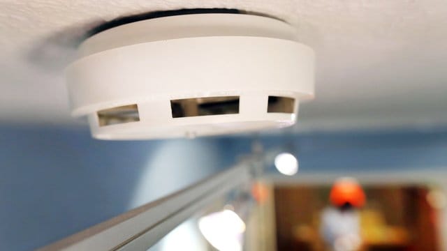Ein Rauchmelder ist an der Decke in einem Hausflur angebracht.