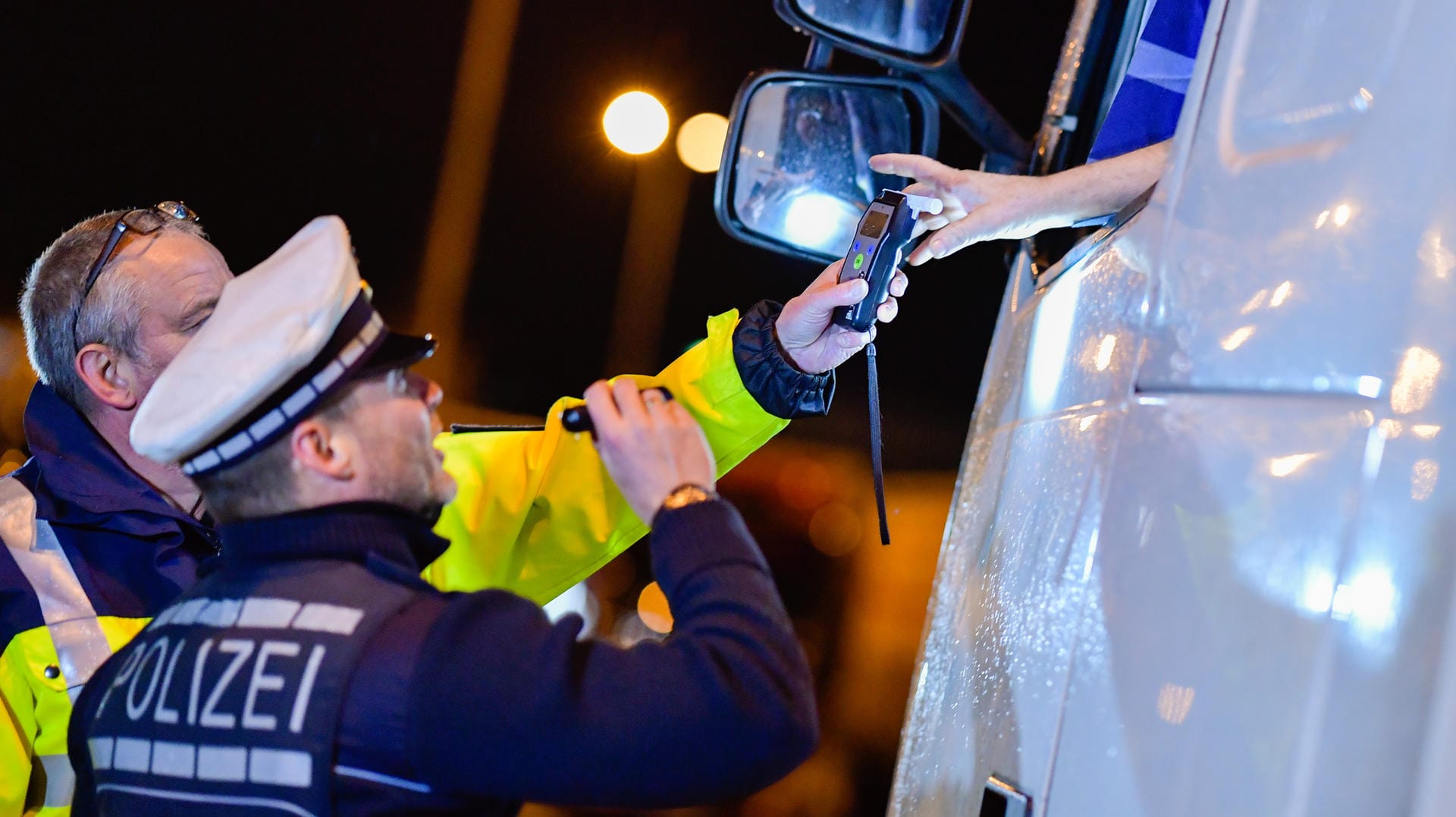 Polizisten reichen ein Alkoholmessgerät in eine Fahrerkabine: Die Polizei geht davon aus, dass dem Sonntagsfahrverbot unterliegende Lkw-Fahrer auf den Rasthöfen teilweise übermäßig Alkohol konsumieren. Polizisten reichen ein Alkoholmessgerät in eine Fahrerkabine: Die Polizei geht davon aus, dass dem Sonntagsfahrverbot unterliegende Lkw-Fahrer auf den Rasthöfen teilweise übermäßig Alkohol konsumieren.