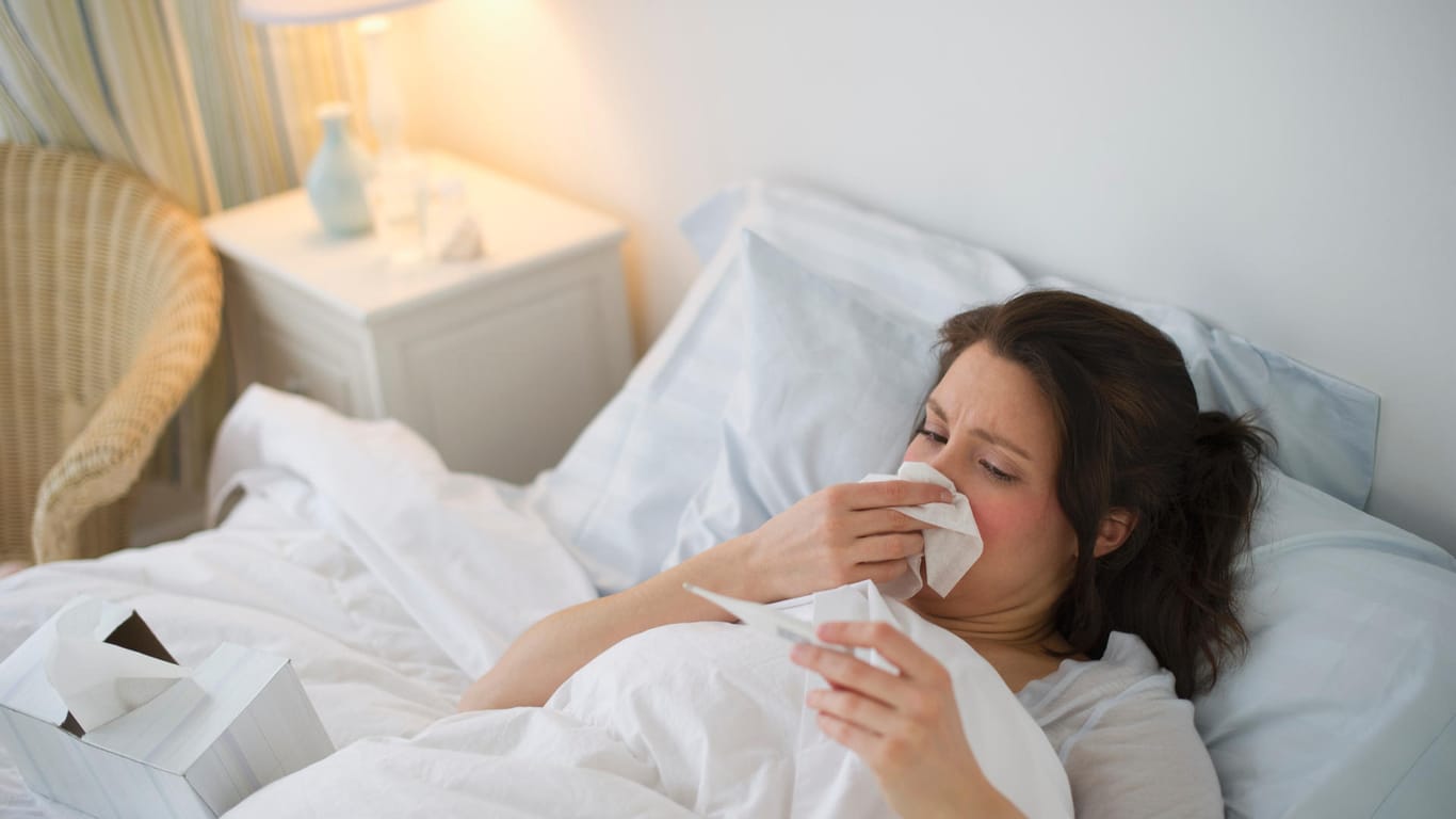 Frau mit Taschentuch und Fieberthermometer im Bett