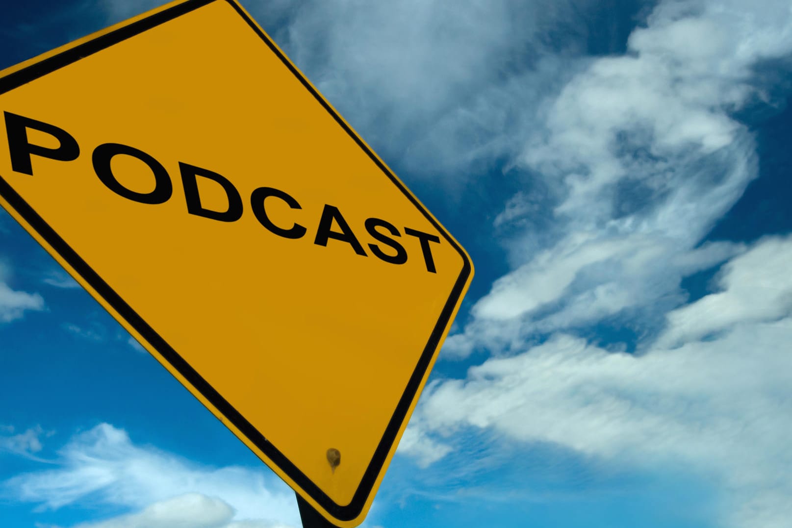 Vor blauem Himmel ist ein rechteckiges, gelbes Verkehrsschild zu sehen, darauf steht in schwarzer Schrift: Podcast