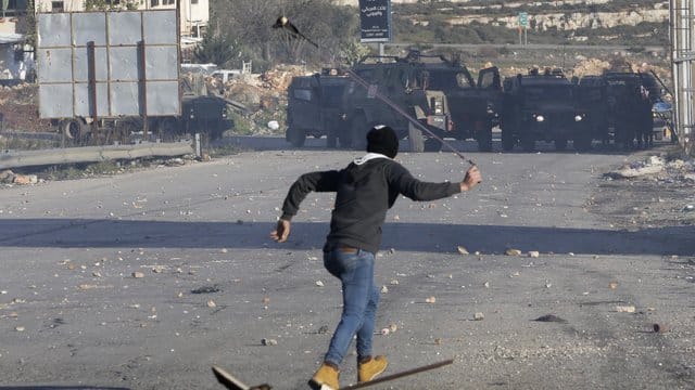 Ein Palästinenser wirft Steine auf israelische Sicherheitskräfte.