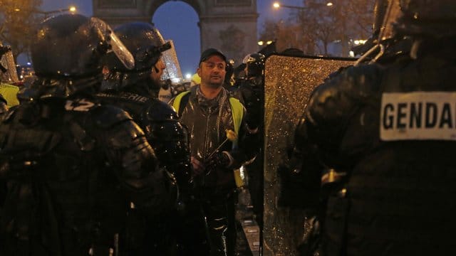 Ein "Geldwesten"-Demonstrant mit einer Blume in der Hand vor Bereitschaftspolizisten.