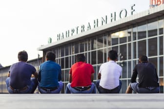 Migranten sitzen auf der Bahnhofstreppe am Kölner Hauptbahnhof: Bei rund einem Drittel der Fälle könnten Asylbewerbern wohl die Leistungen gekürzt werden.