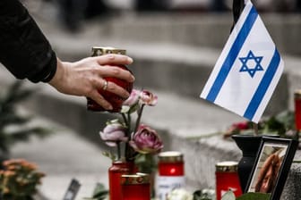 Eine Frau zündet am Breitscheidplatz am Mahnmal vor einer israelischen Fahne ein Kerzenlicht ab.