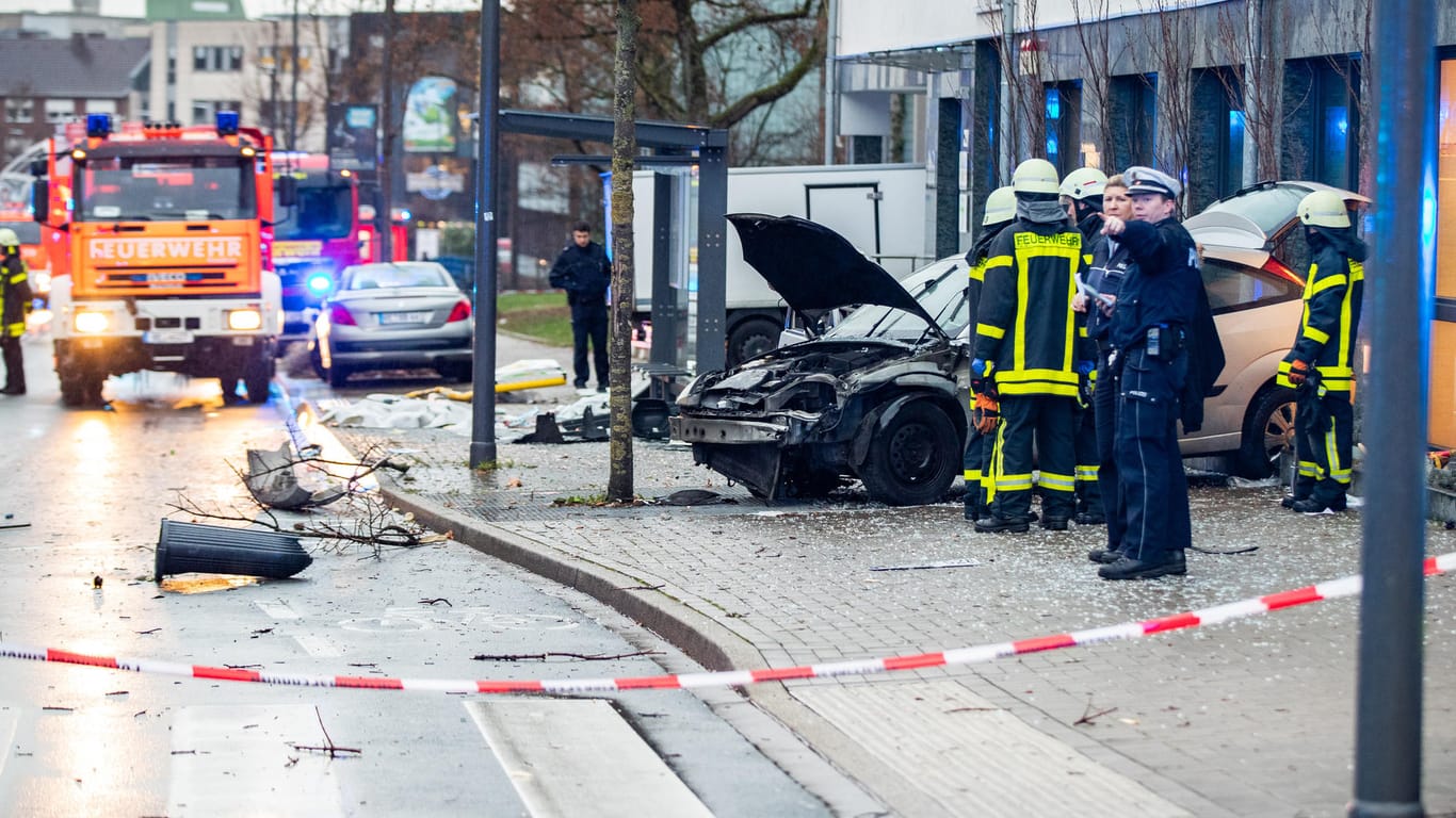 Unfall in Recklinghausen: Polizisten und Feuerwehrleute stehenden neben dem beschädigten Auto an einer Bushaltestelle.