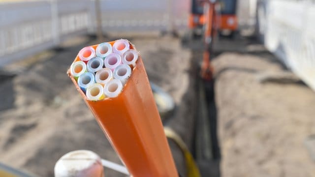 Farbige Leerrohre, in die später Glasfaserkabel verlegt werden, ragen aus dem Graben einer Baustelle.