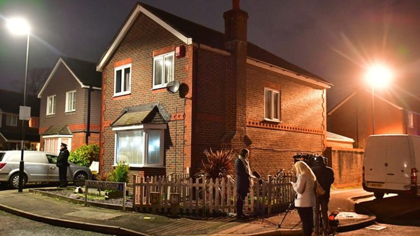 Ein Polizist und ein Kamerateam stehen vor einem Haus, das im Zusammenhang mit dem Drohnenzwischenfall am Flughafen Gatwick durchsucht wurde.