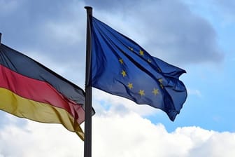Eine Deutschland- und eine EU-Fahne vor wolkigem Himmel.