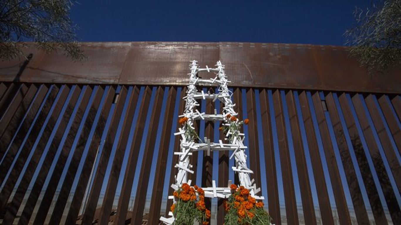 Eine mit Kreuzen und Blumen dekorierte Leiter am Grenzzaun zu den Vereinigten Staaten.