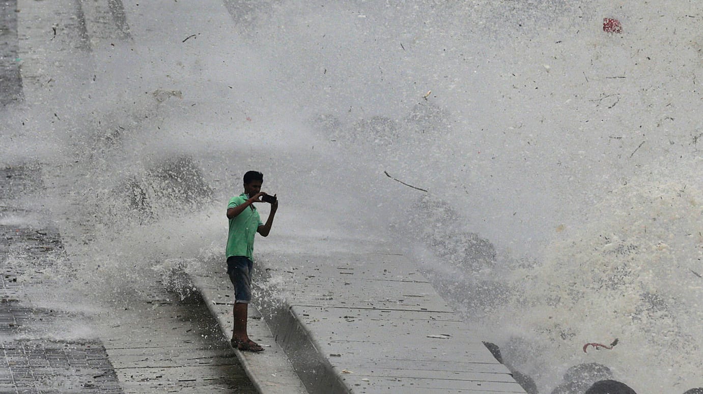 Indien, Mumbai: Ein Mann macht ein Selfie vor einer Welle die über die Promenade spritzt.