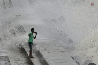 Indien, Mumbai: Ein Mann macht ein Selfie vor einer Welle die über die Promenade spritzt.