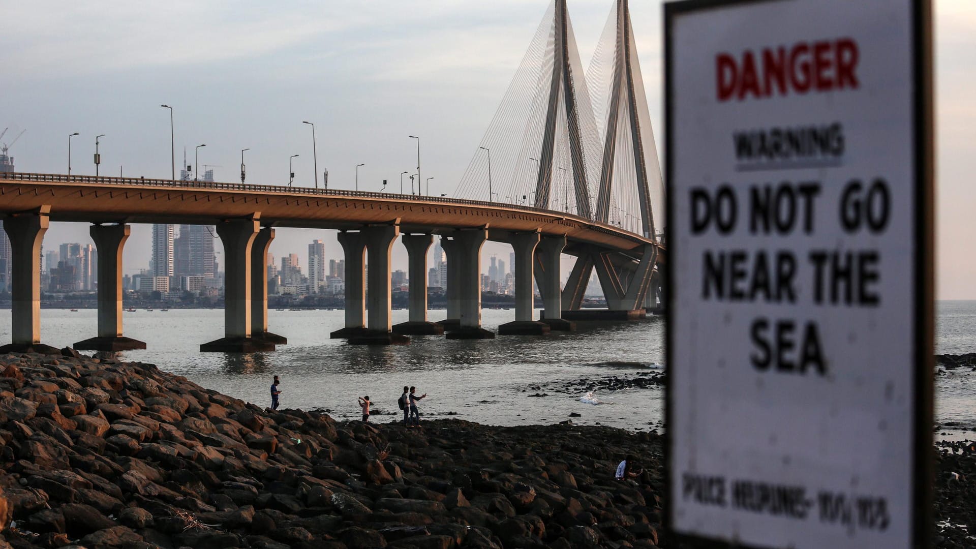 Menschen fotografieren sich am Bandra Fort Band Stand, einem berühmten Touristenort am Arabischen Meer, unweit eines Verbotsschildes, das darauf hinweist, sich von der Wasserkante fern zu halten.