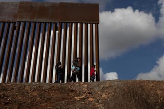 Migranten gehen vor einer Mauer bei Tijuana an der US-Grenze zu Mexiko entlang: Die Demokraten wollen US-Präsident Donald Trump kein Geld für seine komplette Grenzmauer geben.